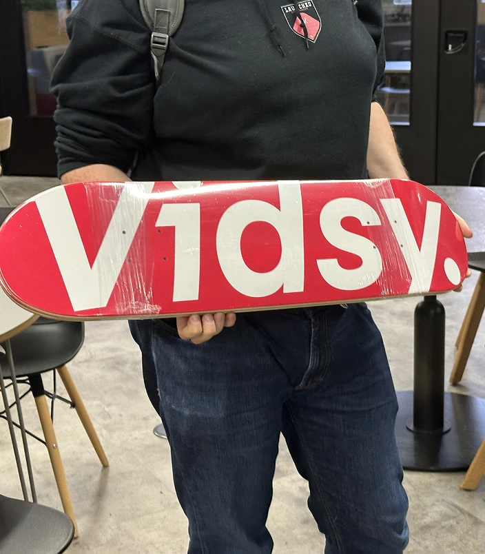 Vidsy team member holding up a red Vidsy-branded skateboard deck